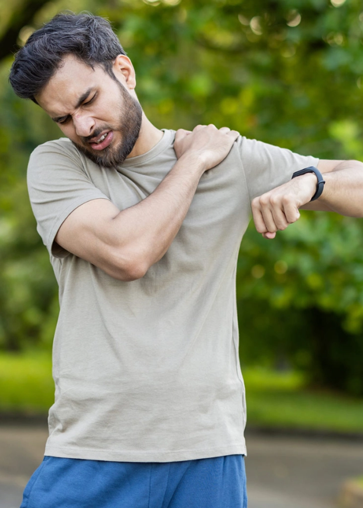 Man holding his shoulder in pain outdoors, representing discomfort that may be addressed with chiropractic adjustments.