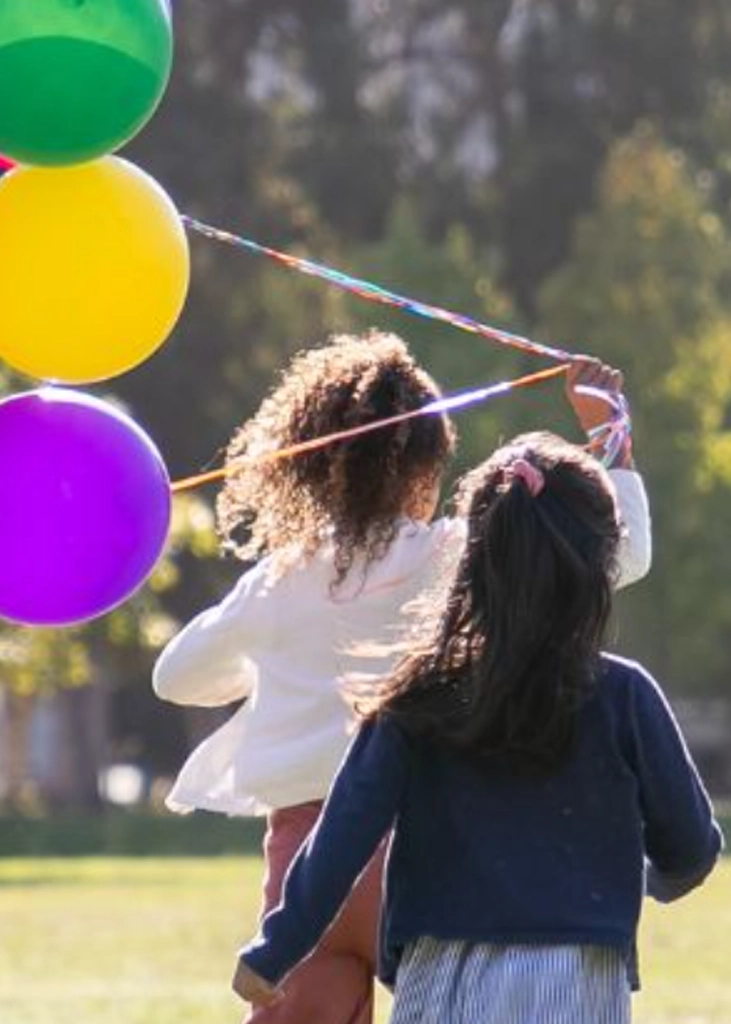 Two children playing outdoors with colorful balloons, representing gentle pediatric chiropractic care and family wellness.