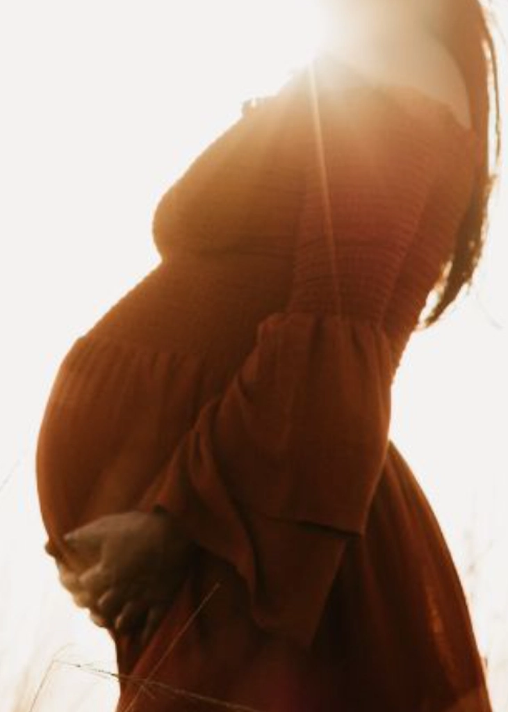 Pregnant woman outdoors holding her baby bump, representing prenatal chiropractic care and pregnancy wellness support.
